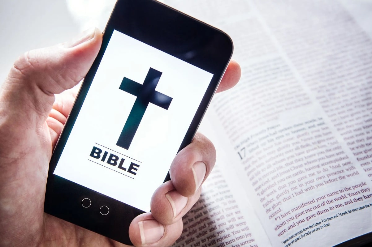 성경책 위에 십자가 화면이 나와 있는 스마트폰을 들고 있는 모습